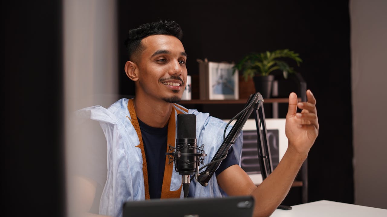 services-04 Smiling young man recording a podcast in a cozy home studio with professional microphone setup.